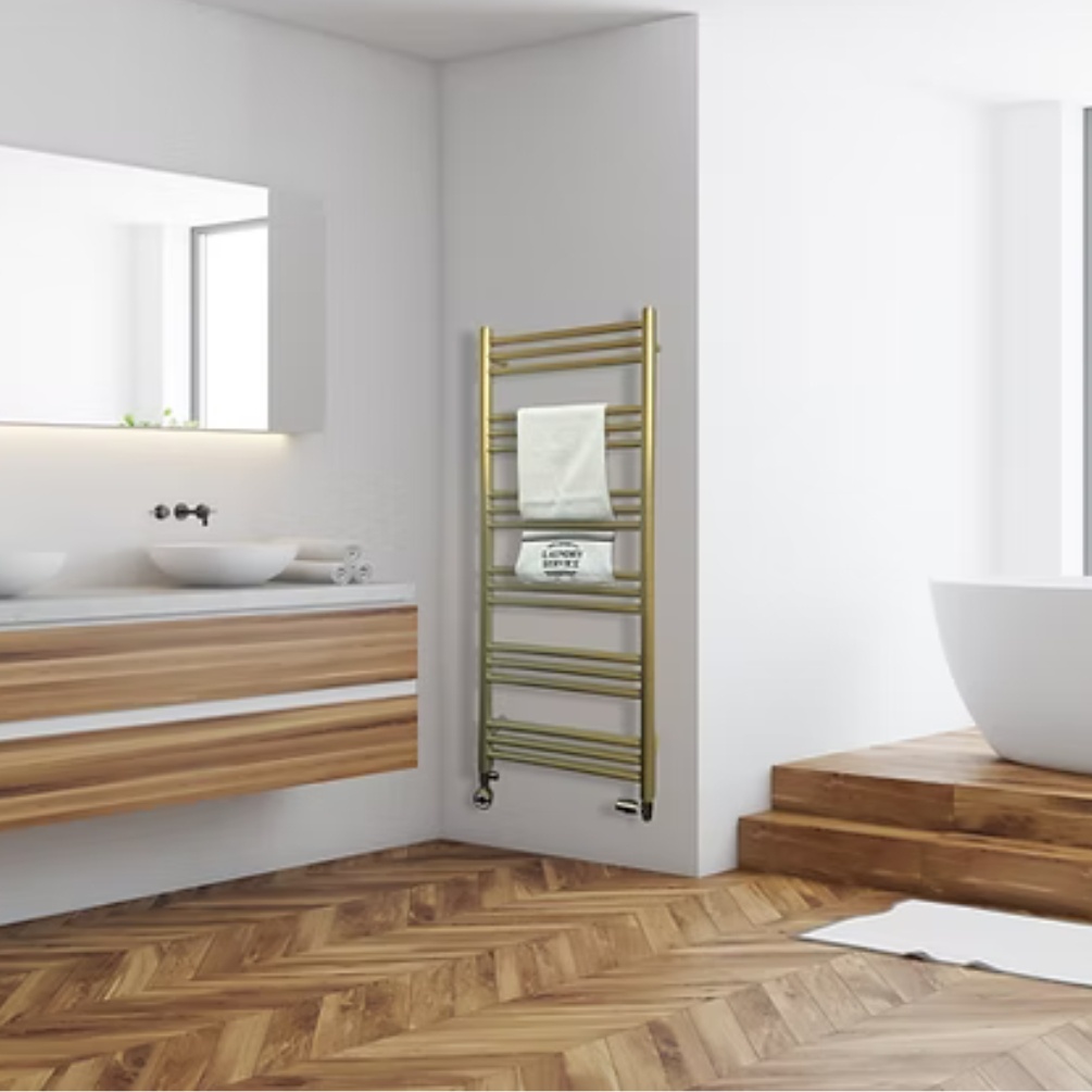 Lifestyle image of the Radox Salento 1210mm Brass Heated Towel Rail mounted on a white bathroom wall, adjacent to a large dual vanity countertop unit with basins